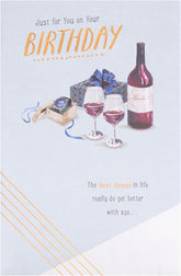 UK Greetings birthday greeting card featuring a watch and wine design with colorful illustrations and festive elements.