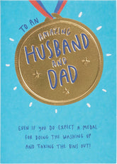 UK Greetings Father's Day card for husband or dad featuring a gold medal design, with colorful and festive artwork.