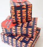 Bright birthday greeting card from Abacus Cards featuring colorful "Happy Birthday" design with matching gift wrap sheets and tags.