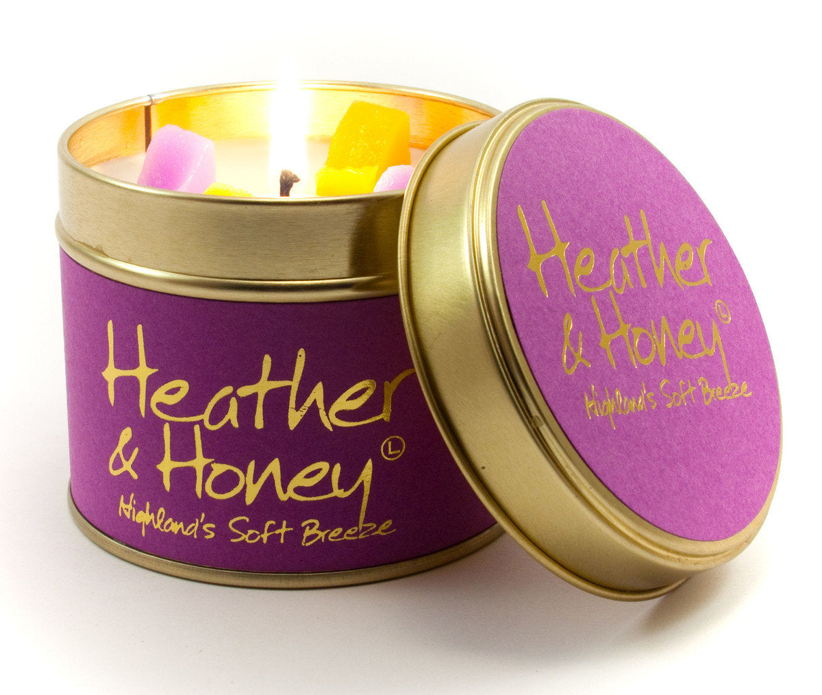 Lily-Flame Heather & Honey scented tin candle with a decorative label and a lit wick, in a small, round metal container.