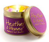 Lily-Flame Heather & Honey scented tin candle with a decorative label and a lit wick, in a small, round metal container.